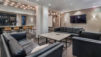 A modern lounge area with leather sofas, a coffee table, and a flat-screen TV mounted on the wall.