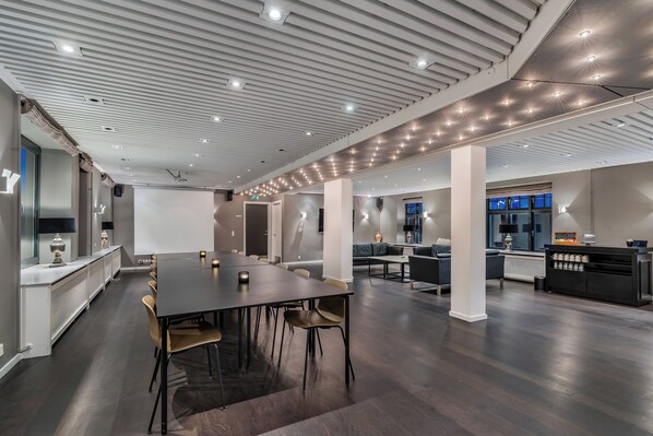 A modern conference room with a long table, chairs, and a projector screen.