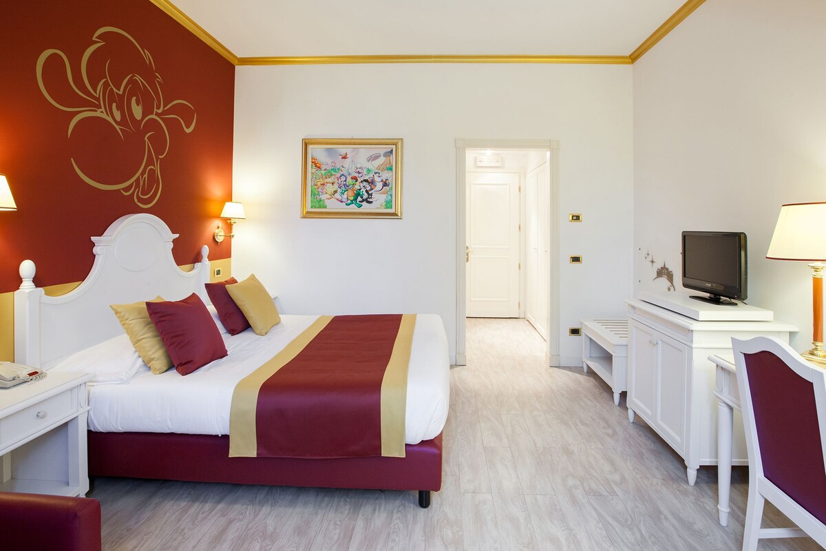 Une chambre d’hôtel comprenant un lit, une table de chevet, une lampe, une télévision et une porte donnant sur une autre pièce.