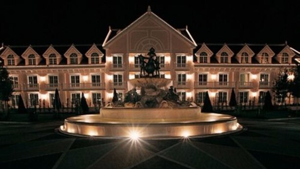 A large, illuminated building with a central fountain and statues, surrounded by symmetrical architecture. - Gardaland Hotel (Castelnuovo del Garda)