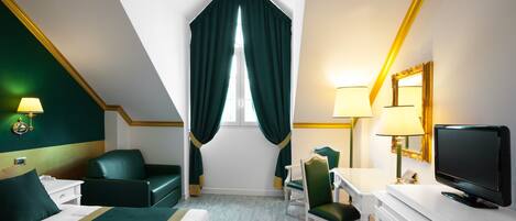 A hotel room with a bed, a desk with a chair, a television, and a window with curtains.