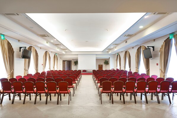 A conference room with rows of red chairs, a podium, and a large screen.