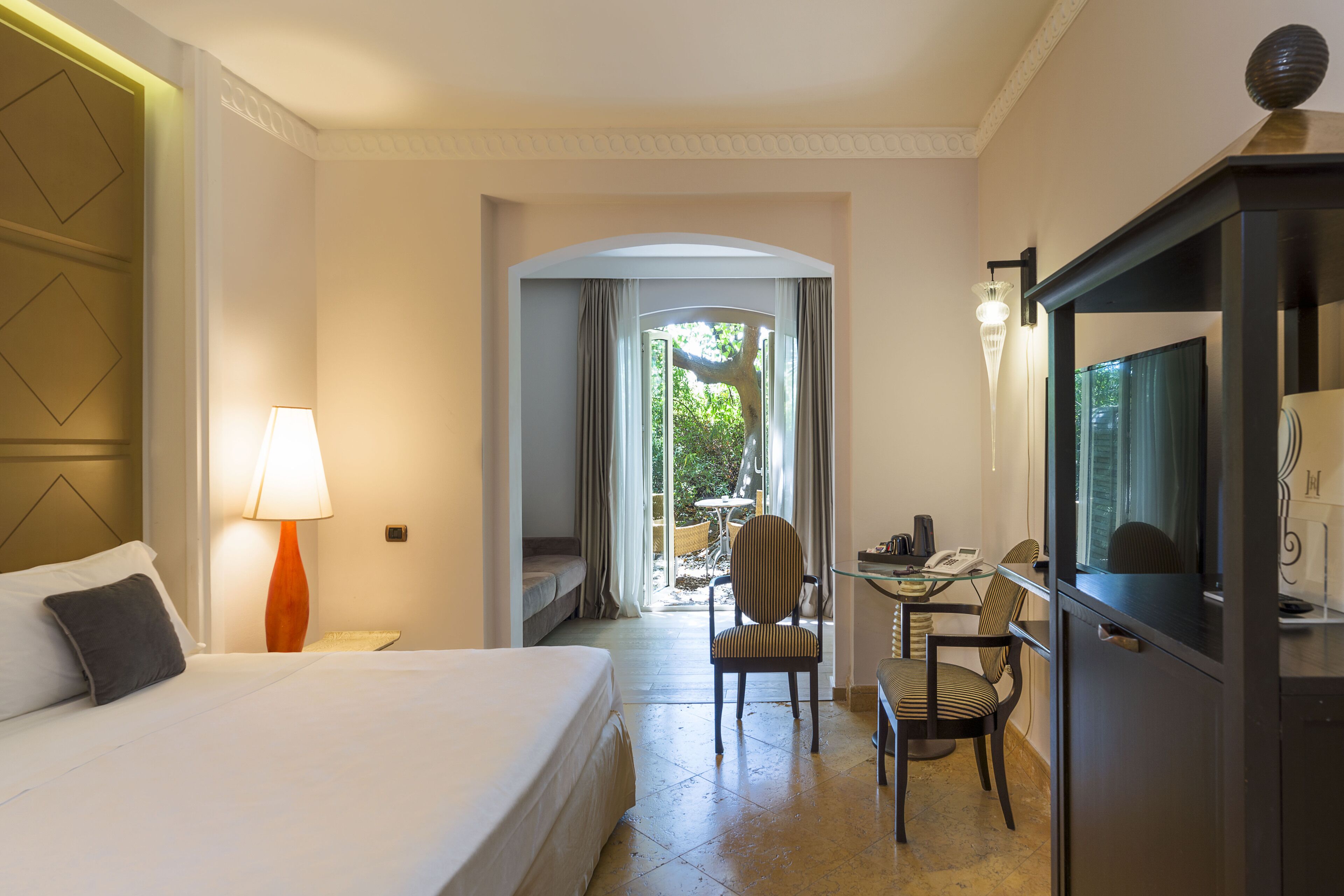 A hotel room with a bed, a desk with a chair, a lamp, and a television.