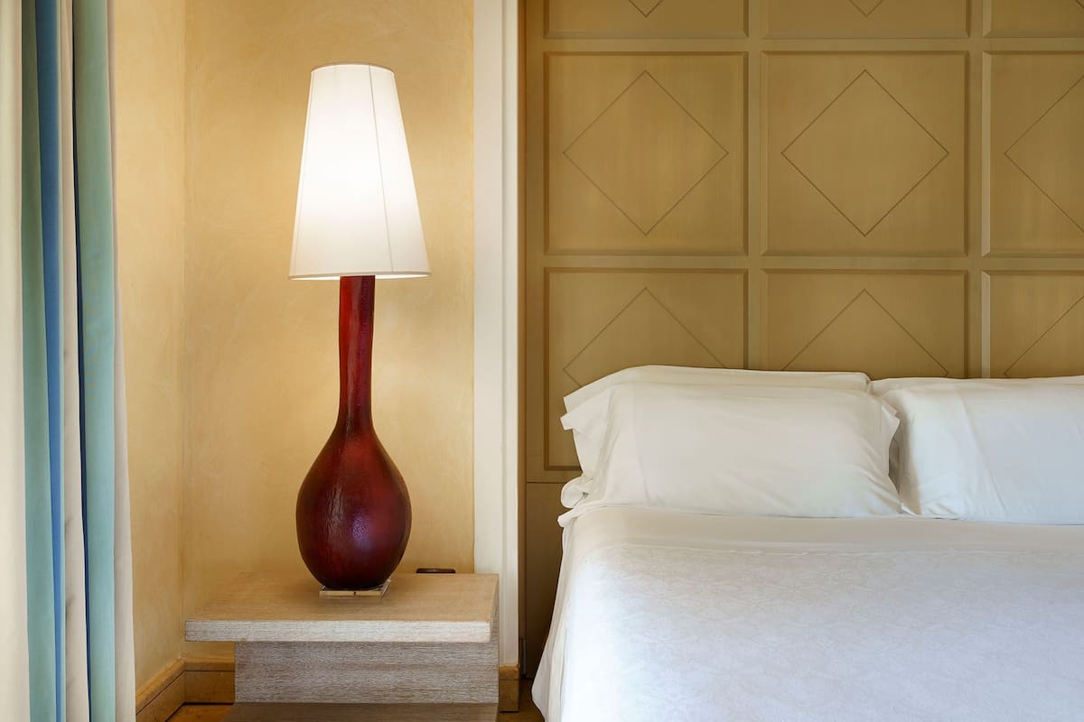 Ein Hotelzimmer mit Bett, Nachttisch mit Lampe und Wand mit geometrischem Muster.