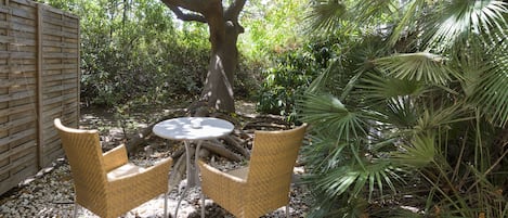 An outdoor seating area with two wicker chairs and a small round table, surrounded by pebbles and greenery.