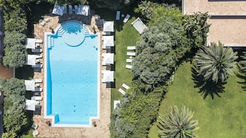 An aerial view of a swimming pool surrounded by lounge chairs and umbrellas, with lush greenery and palm trees.