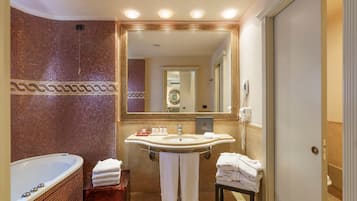A bathroom with a large mirror, a bathtub, a sink with toiletries, and towels.