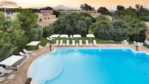 A swimming pool with lounge chairs and umbrellas, surrounded by greenery and buildings in the background.