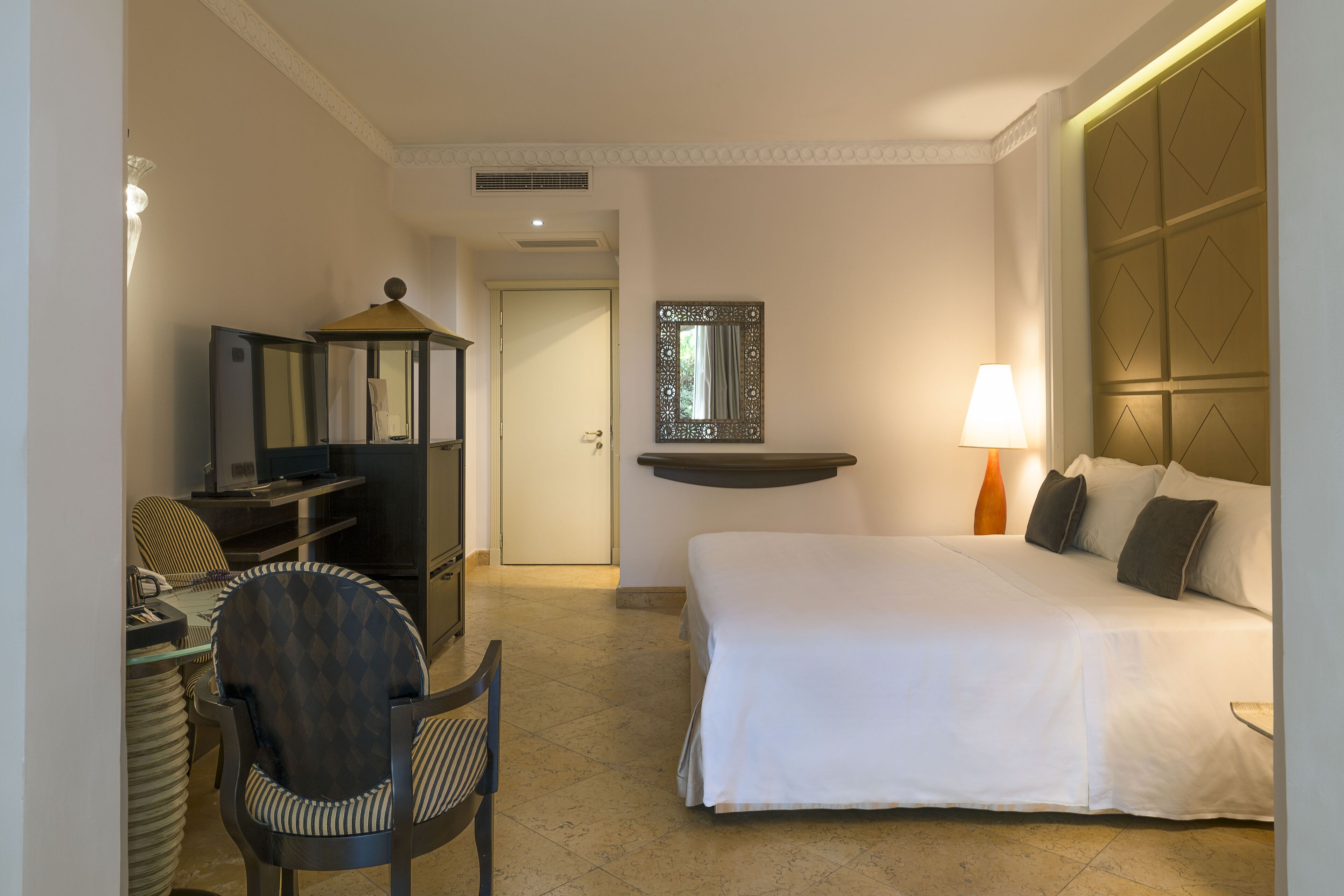 Una habitación de hotel con una cama, un escritorio con una computadora, una silla, una lámpara y un espejo.
