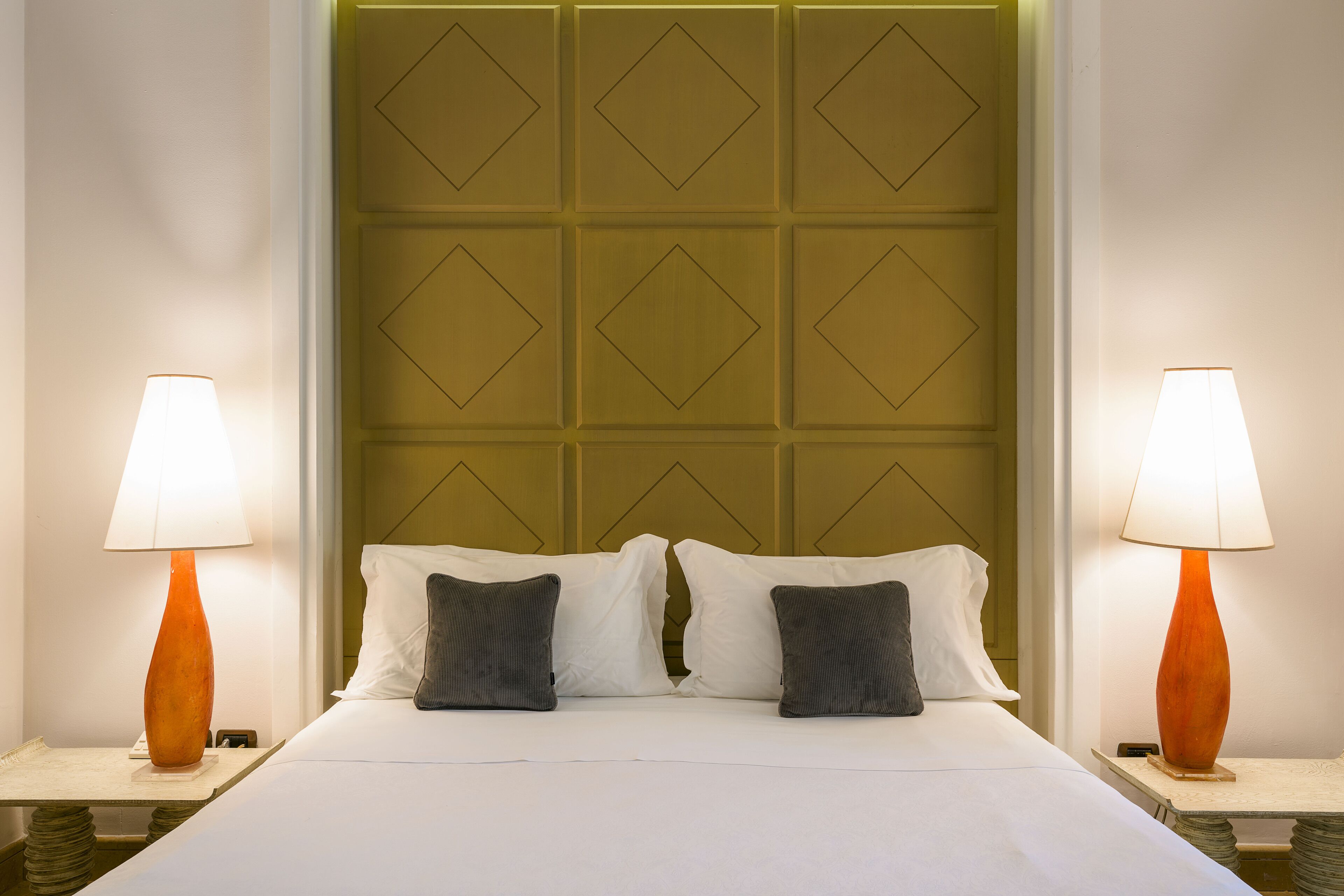 A hotel room with a neatly made bed, two bedside lamps, and a headboard with a geometric pattern.