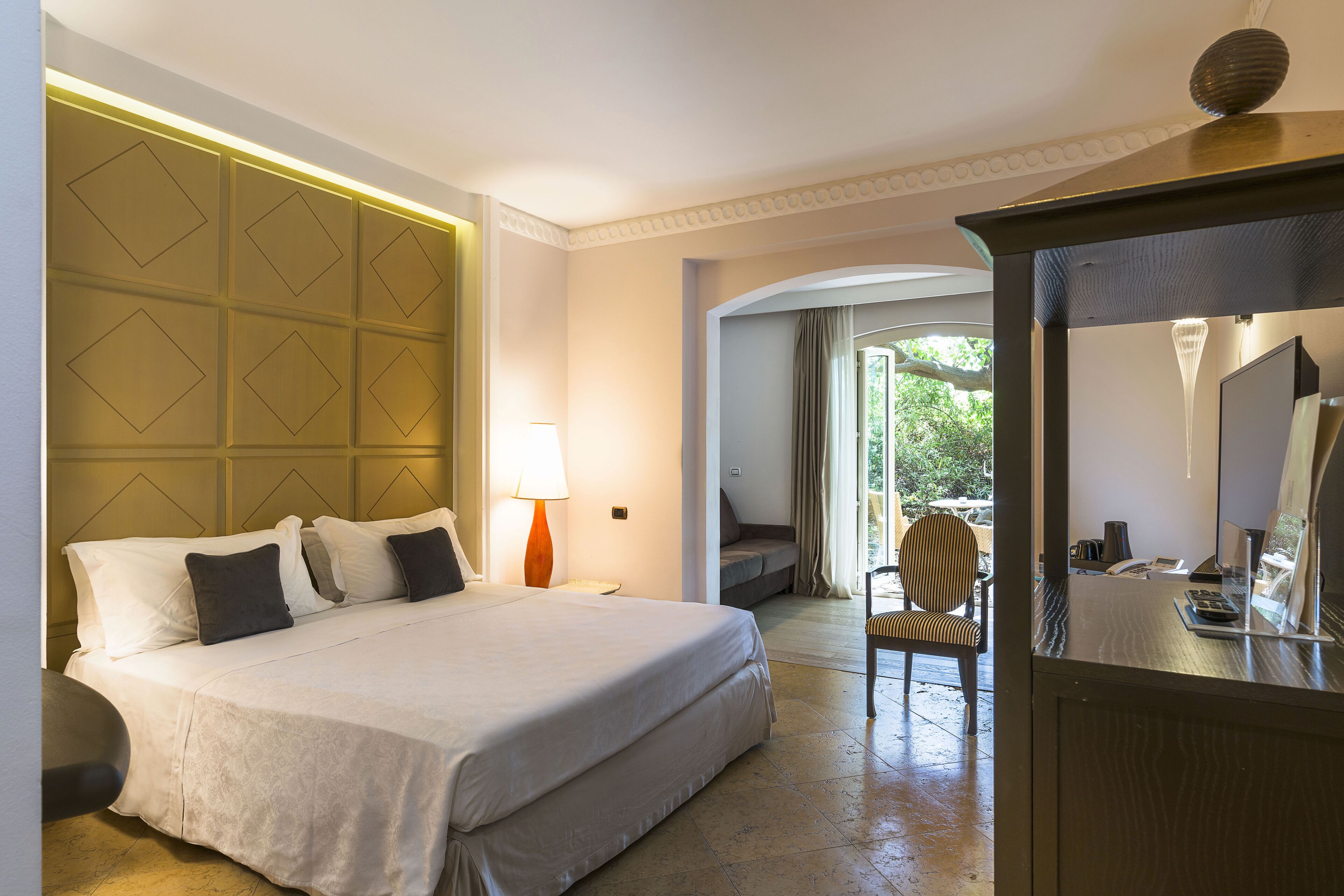 Ein Hotelzimmer mit einem großen Bett, einem Schreibtisch mit Spiegel und Blick ins Freie.