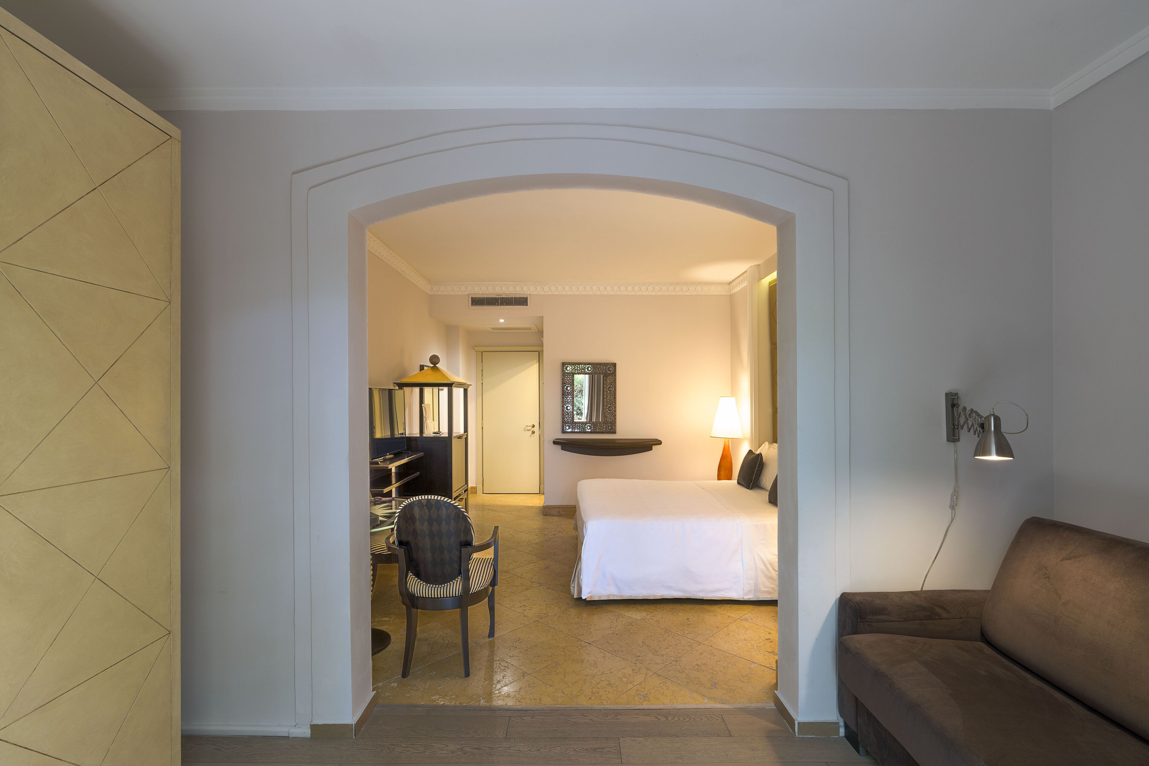 A hotel room with a bed, a desk, a chair, a sofa, and a lamp.