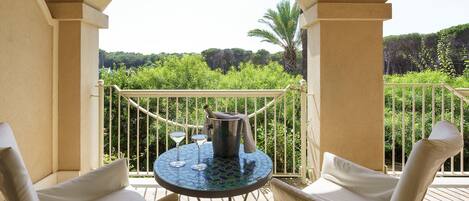 A balcony with a table, two chairs, and a view of lush greenery.