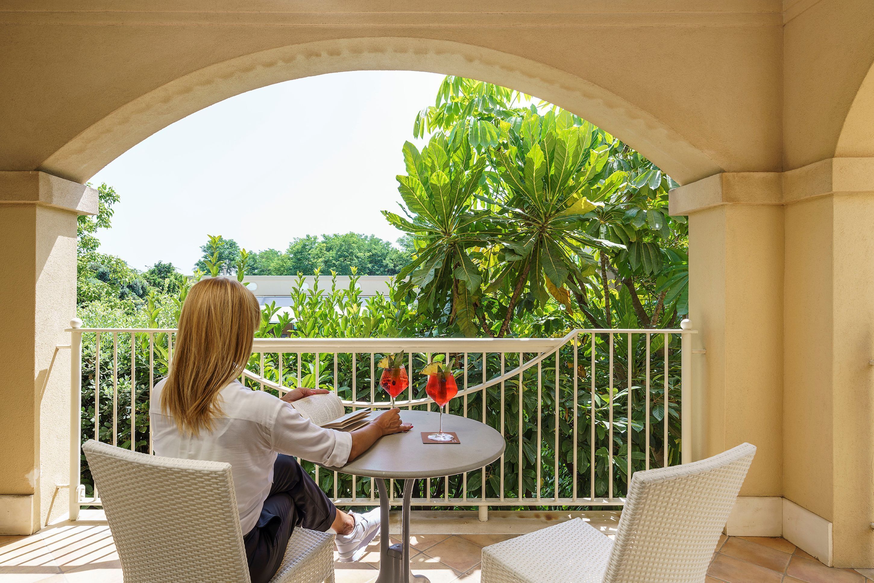 A balcony with a white railing, a round table, and two wicker chairs.
