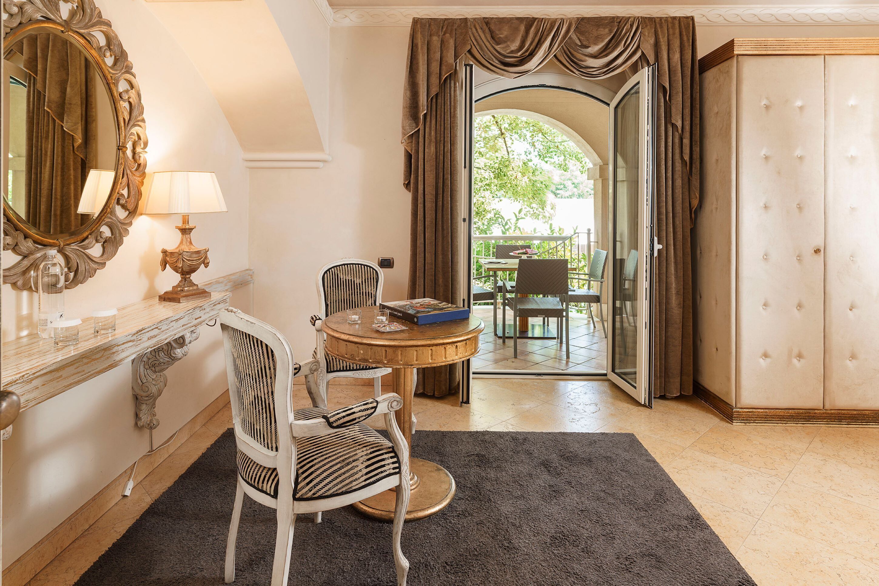 A room with a round table, two chairs, a mirror, and a wardrobe.