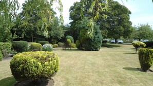 A well-maintained garden with neatly trimmed hedges, a bench, and a variety of trees. - Park Hotel (Montrose)