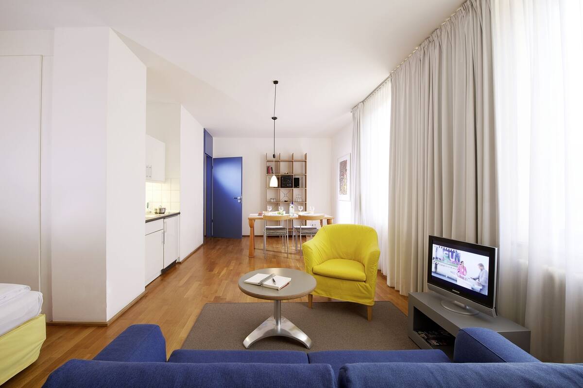 Una habitación de hotel moderna con sofá, televisor, zona de comedor y cocina.