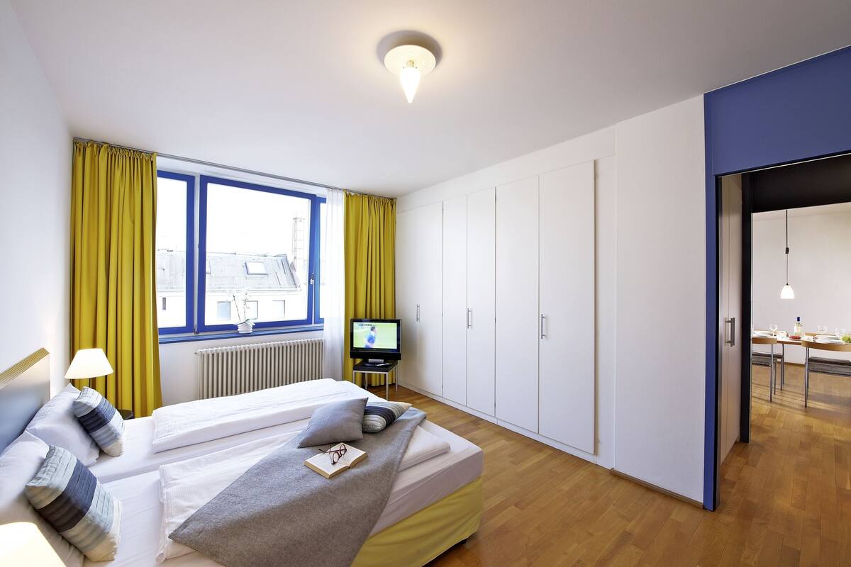 Una habitación de hotel moderna con una cama, un televisor y vistas a la ciudad a través de amplios ventanales.
