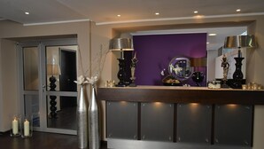 A reception area with a wooden counter, a purple wall, and a glass door. - Hotel Medo Köln (Cologne)
