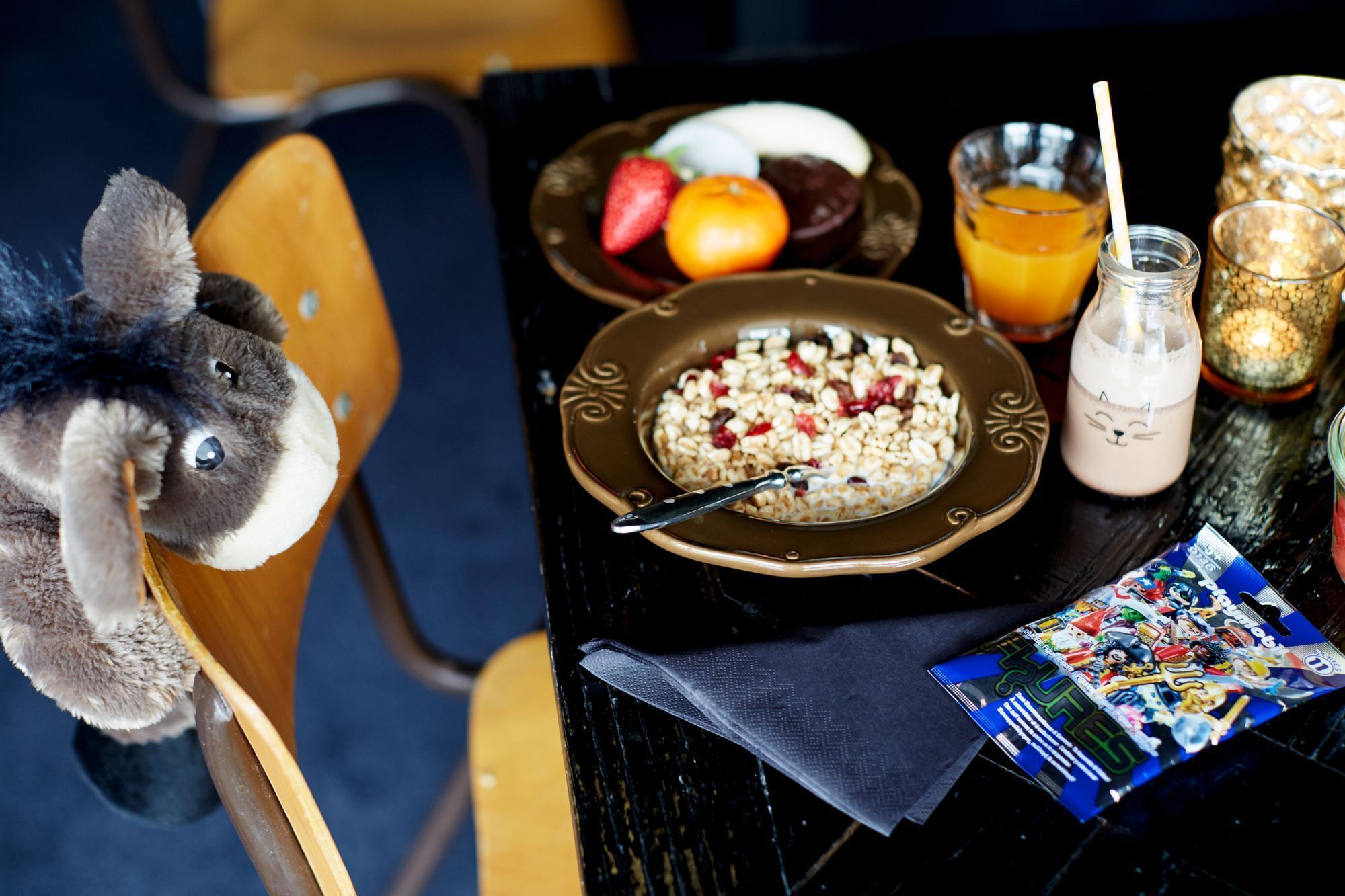 Una mesa de comedor con un plato de cereal, un vaso de jugo de naranja, una botella de leche y un peluche.