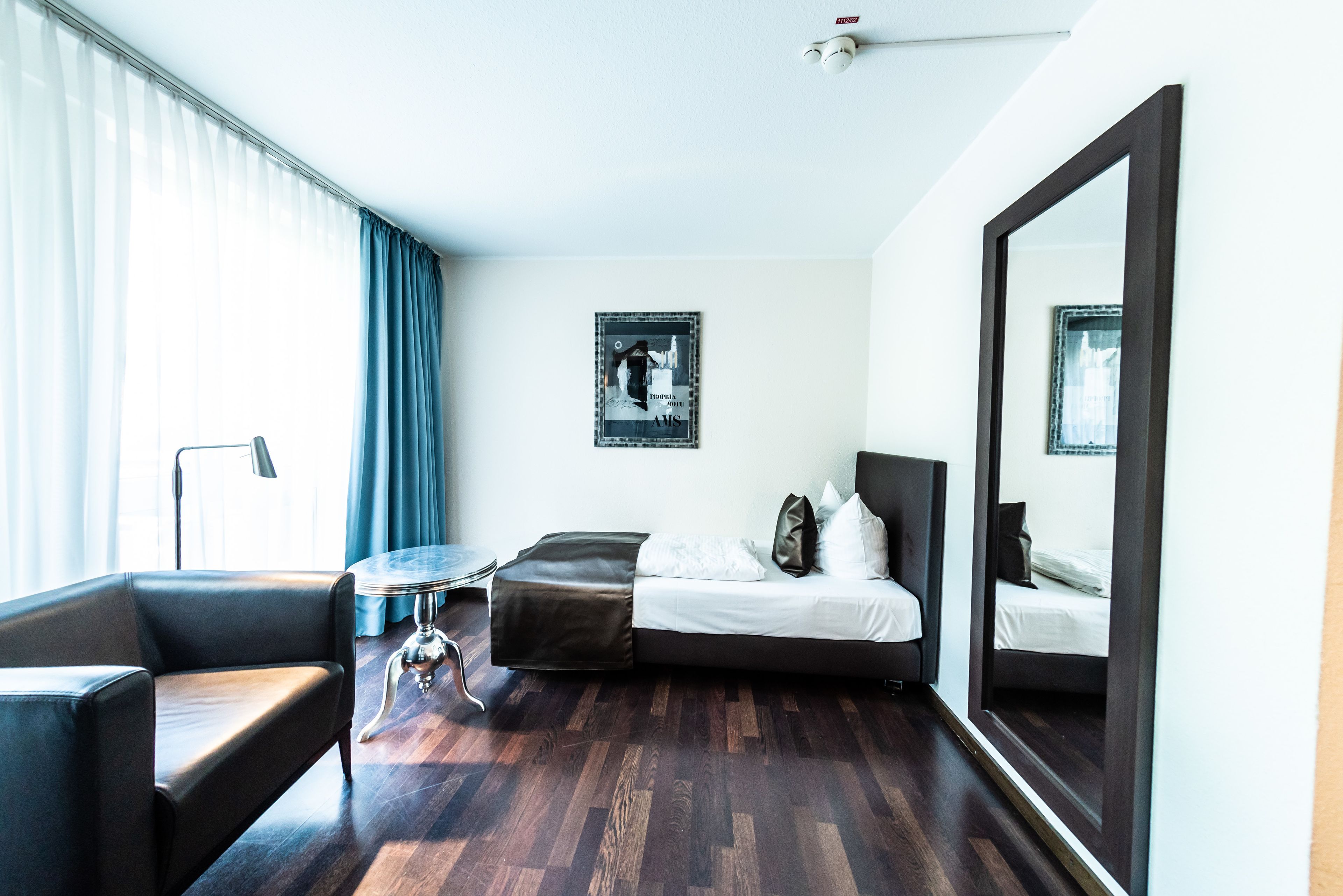 A modern hotel room with a bed, a sofa, a small table, and a large mirror.