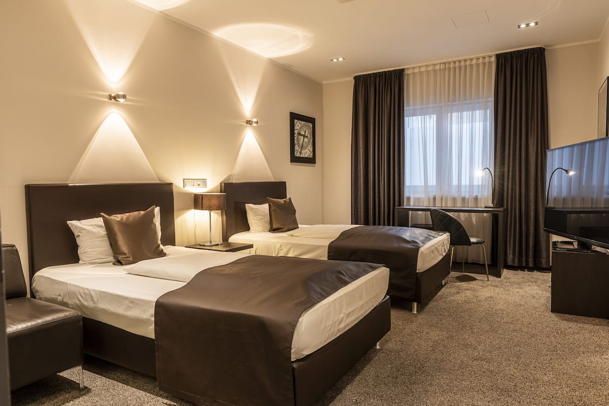 Une chambre d’hôtel avec deux lits, un bureau, une chaise, une télévision et une horloge au mur.