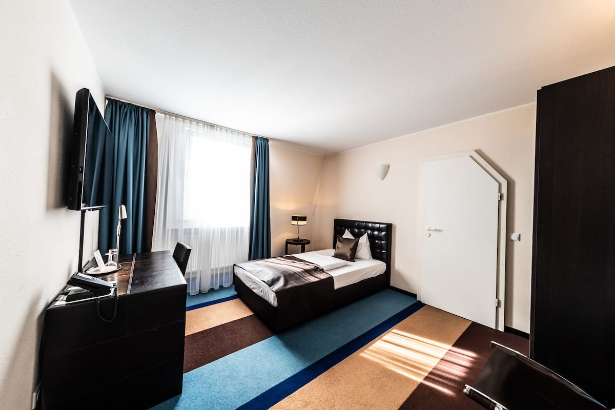 Une chambre d’hôtel comprenant un lit, un bureau avec une chaise, une lampe et une armoire.