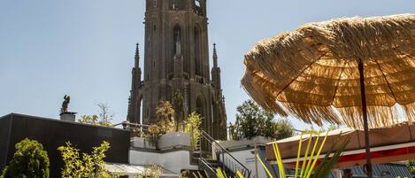 A cathedral with a tall spire, outdoor seating with wicker furniture, and a large thatched umbrella.