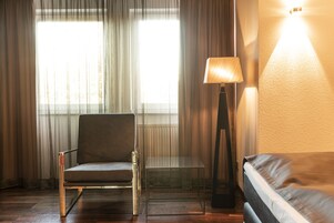 Una habitación con una silla, una mesita, una lámpara de pie y una cama.