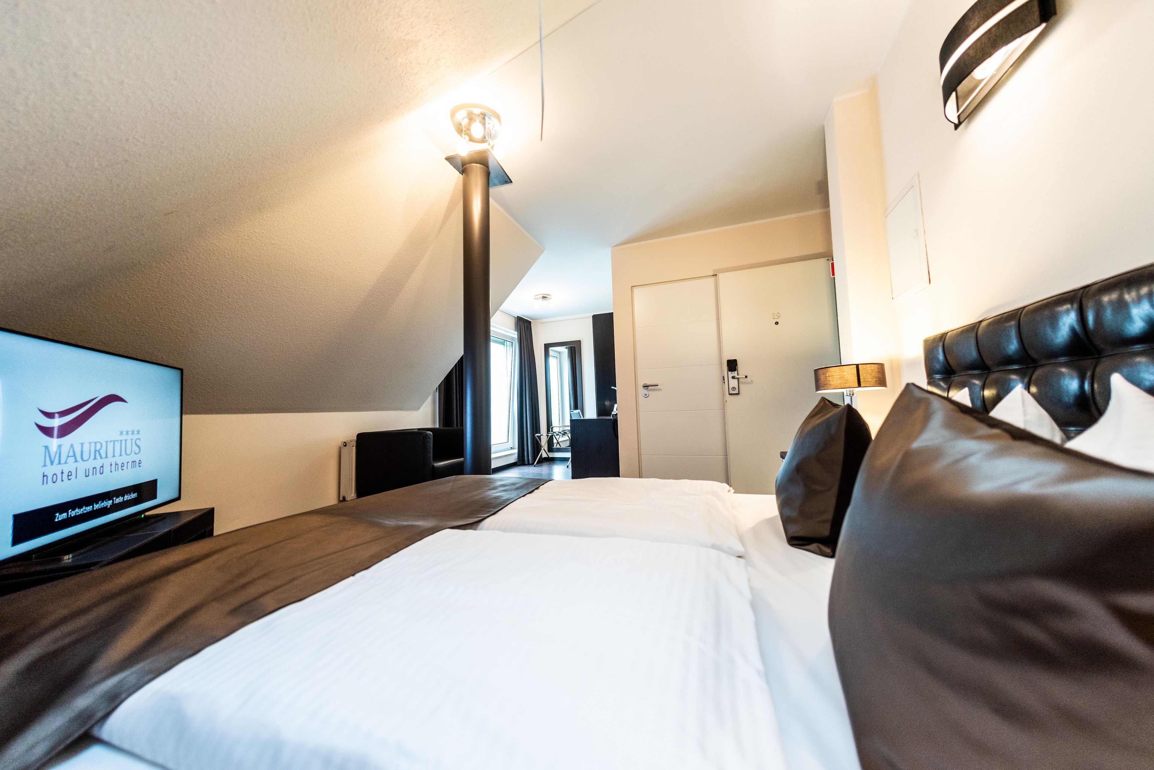 Ein Hotelzimmer mit Bett, Fernseher mit dem Hotelnamen, Schreibtisch und Lampe.