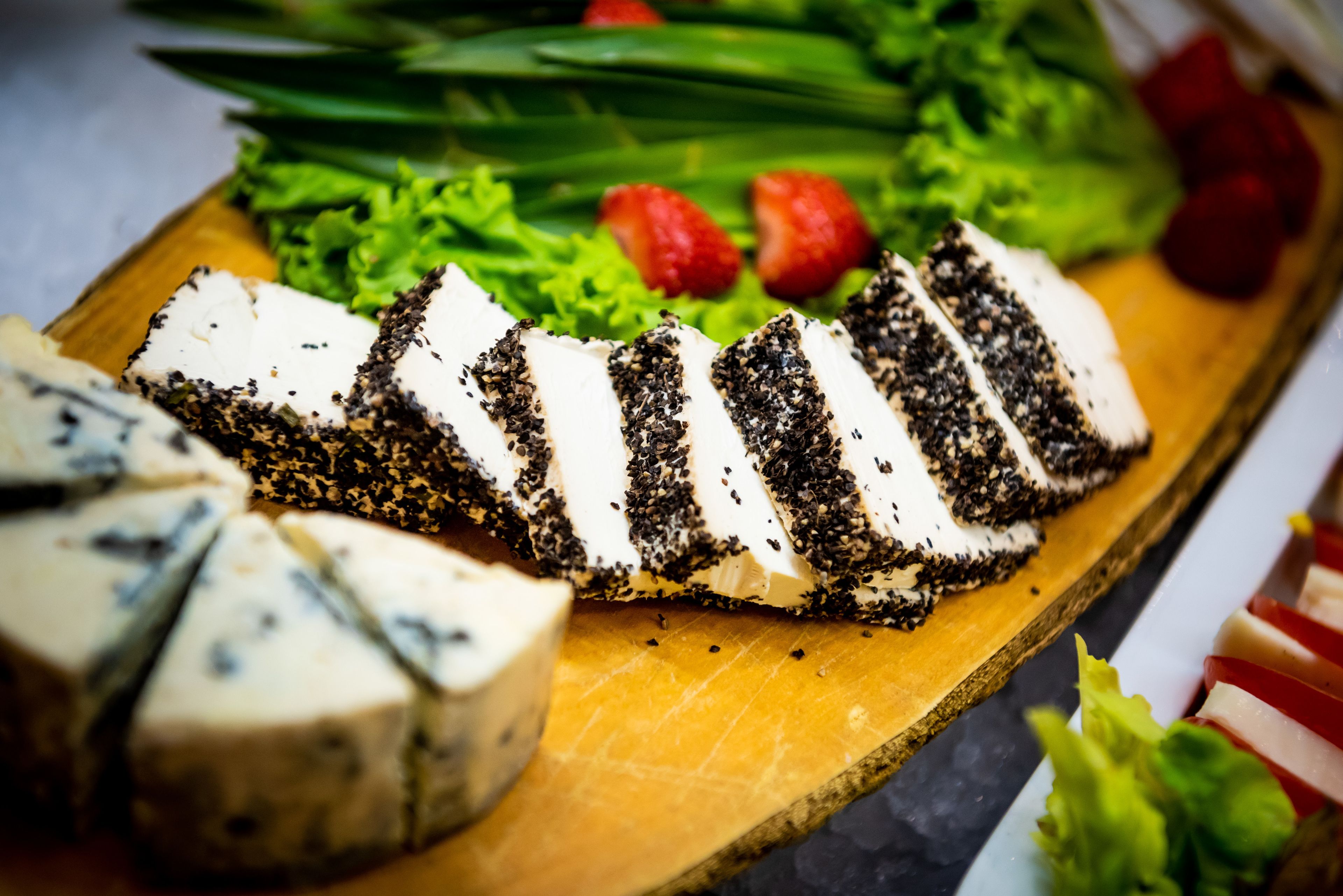 Une planche en bois garnie de fromage en tranches, de fraises et de laitue.