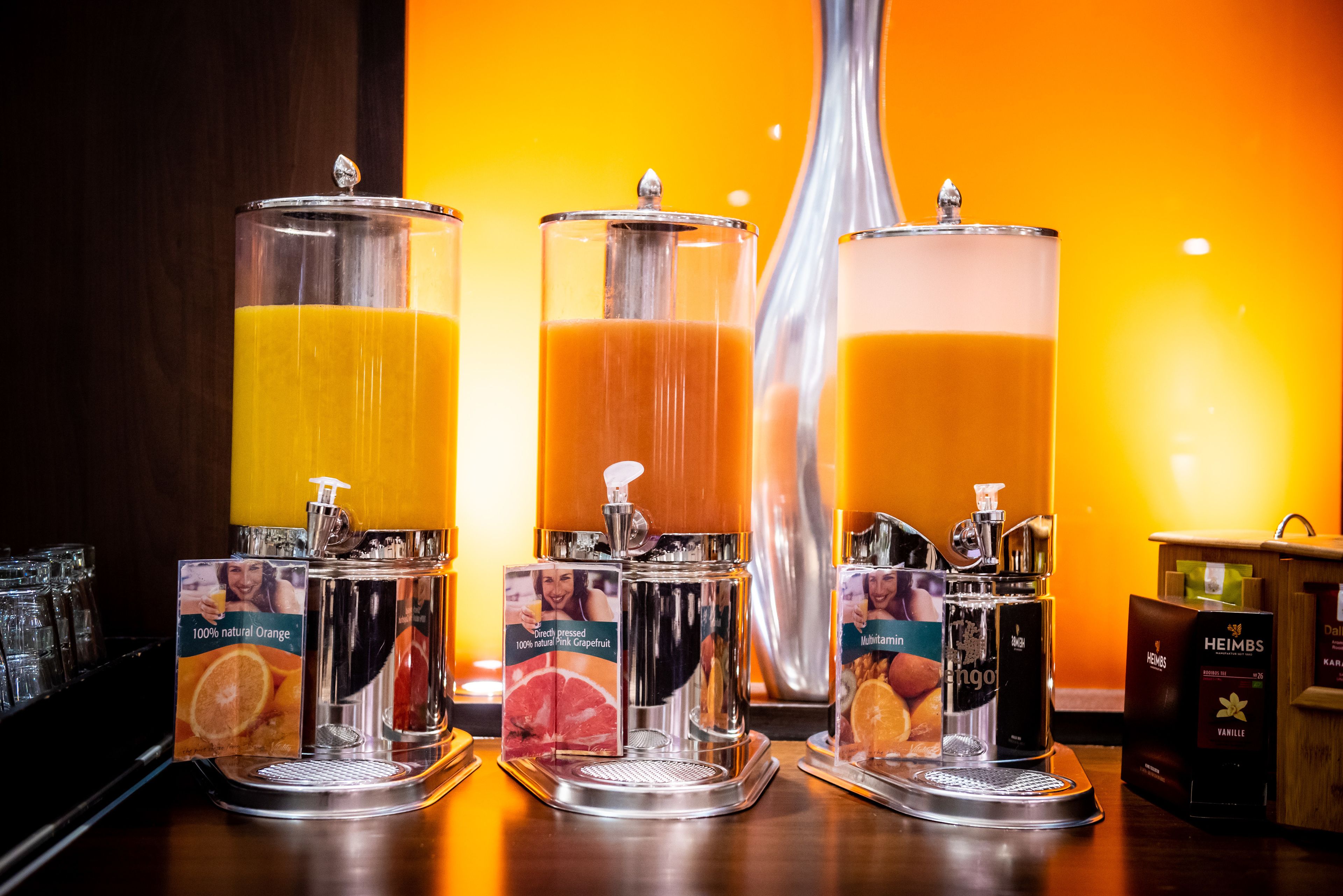 Drei Saftspender mit Beschriftungen für Orange-, Grapefruit- und Mangogeschmack.