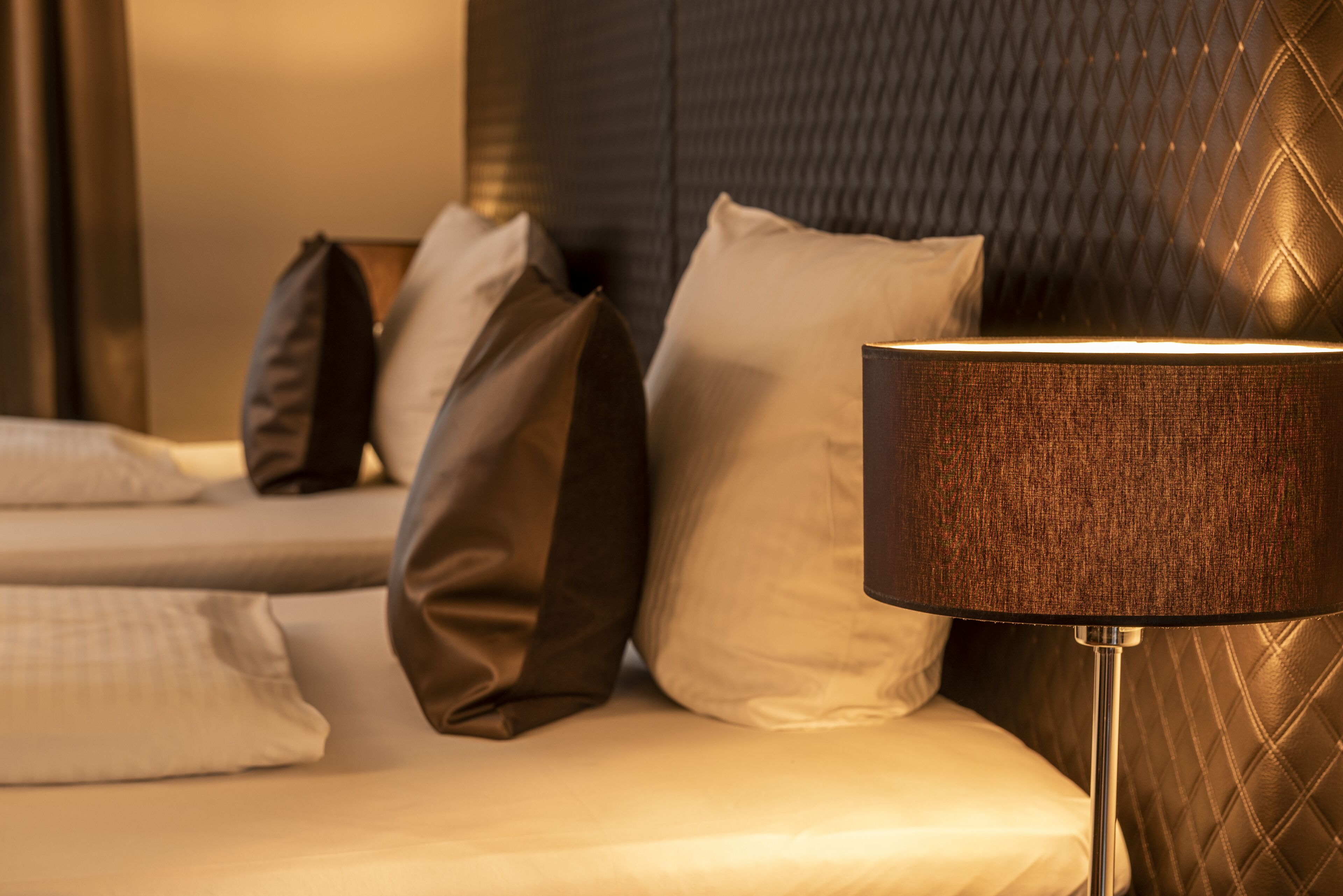 Quarto de hotel com cama, almofadas e luminária.
