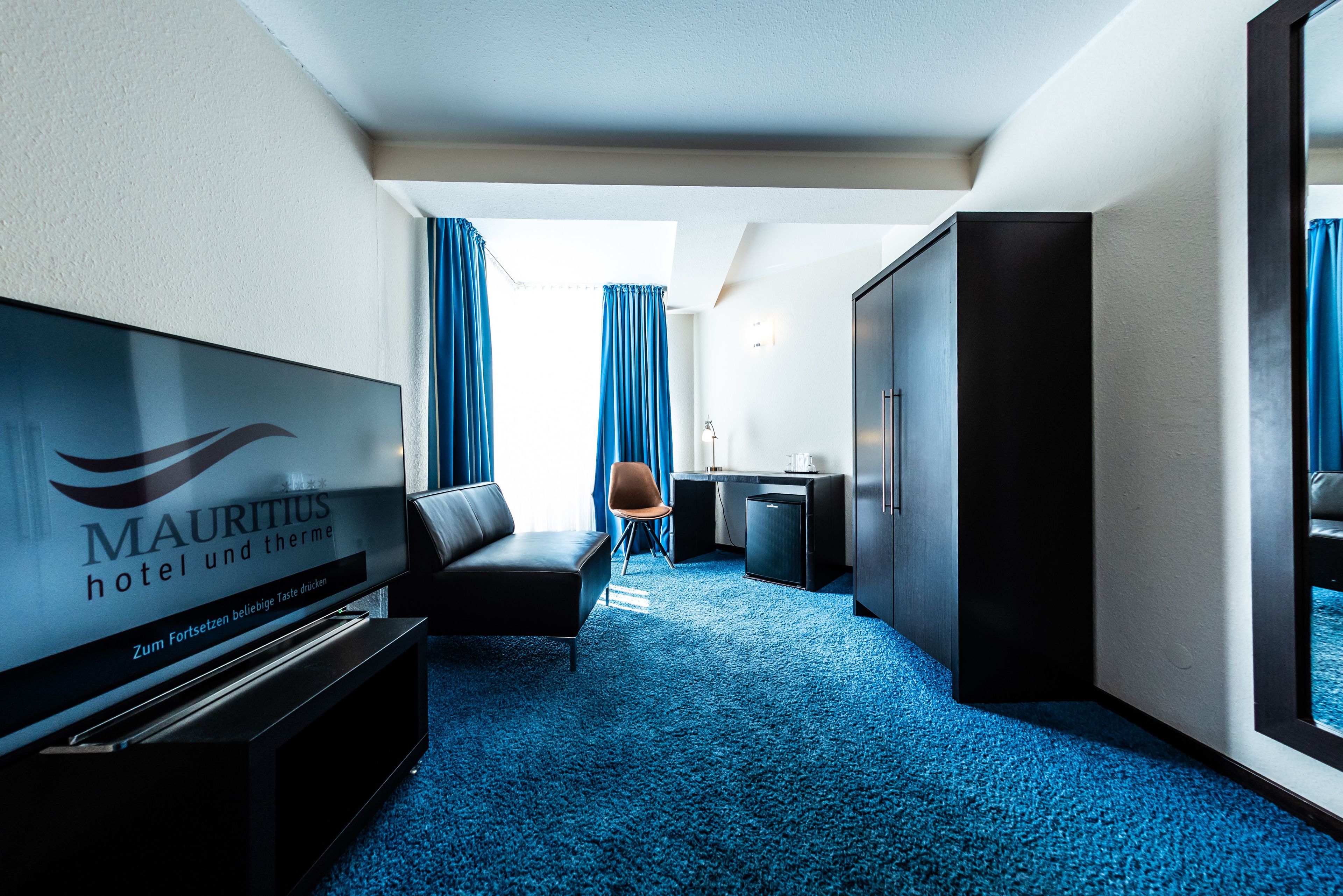 Habitación de hotel con televisor de pantalla plana, sofá, escritorio y minibar.