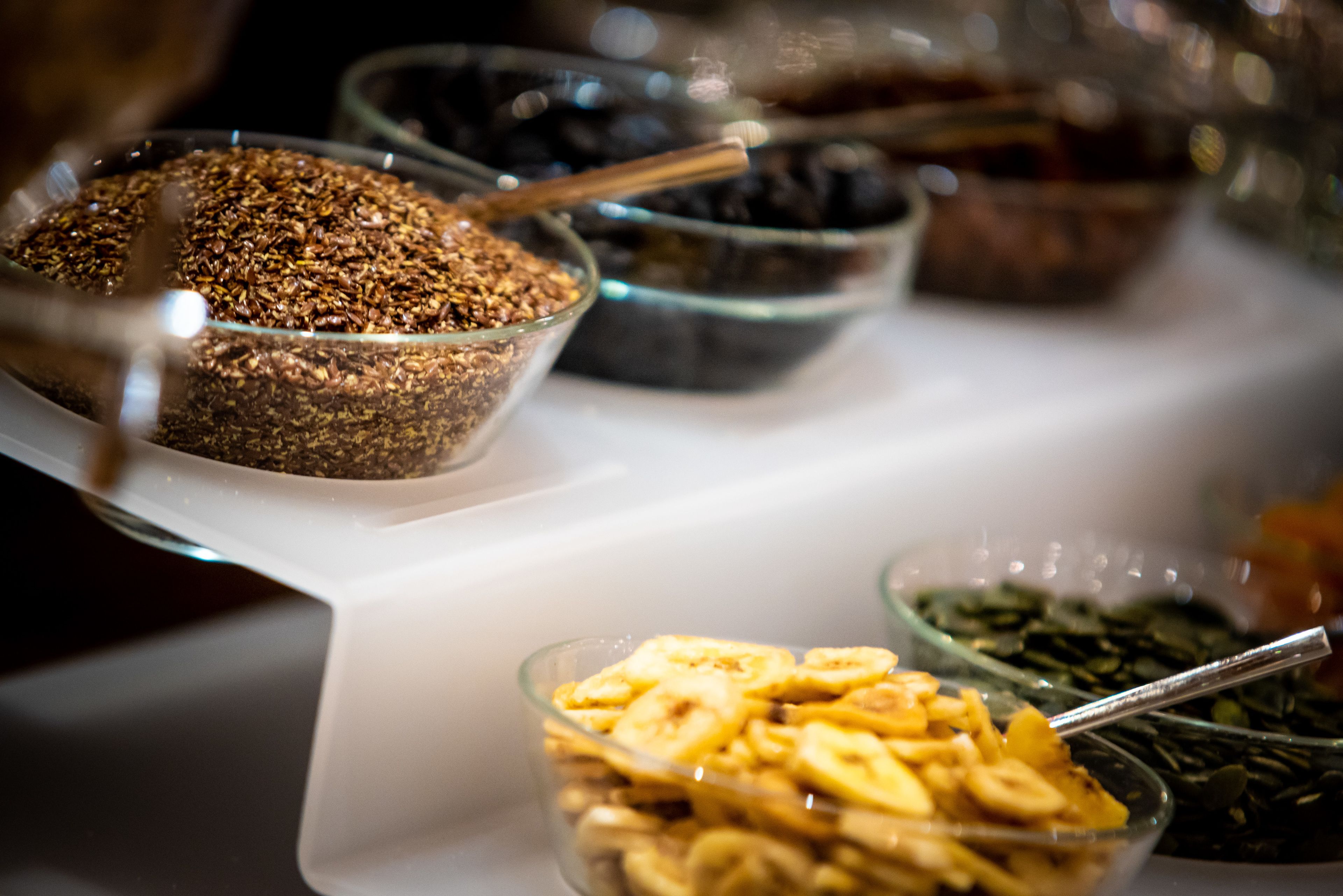 Un buffet con diversi cibi esposti in ciotole di vetro, tra cui sembrano esserci granola, noci e banane a fette.
