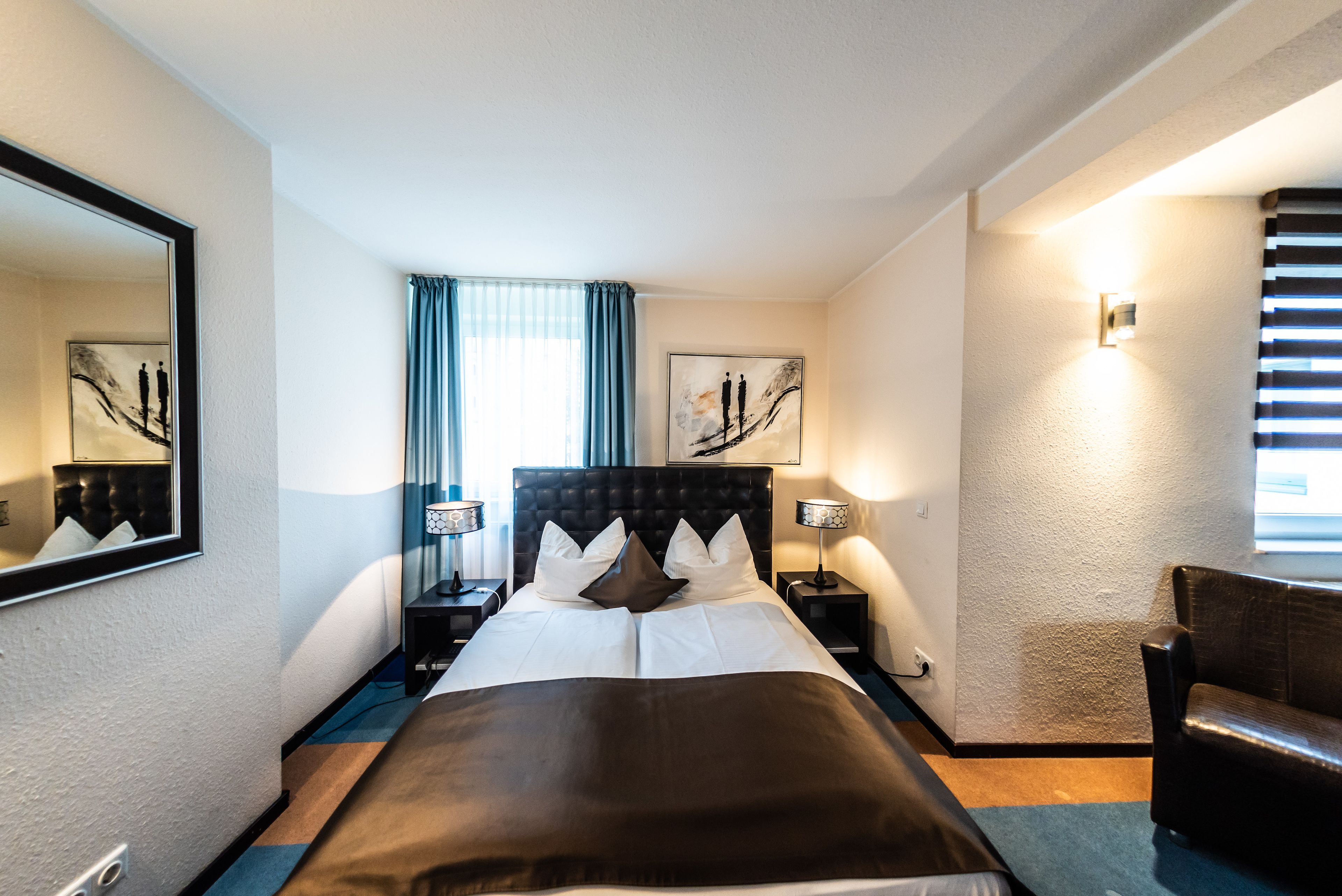 Una habitación de hotel con una cama grande, dos mesitas de noche con lámparas, una silla y obras de arte en las paredes.