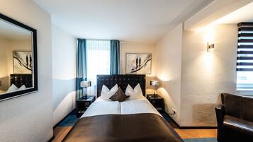 Ein Hotelzimmer mit einem großen Bett, zwei Nachttischen mit Lampen, einem Sessel und Bildern an den Wänden.