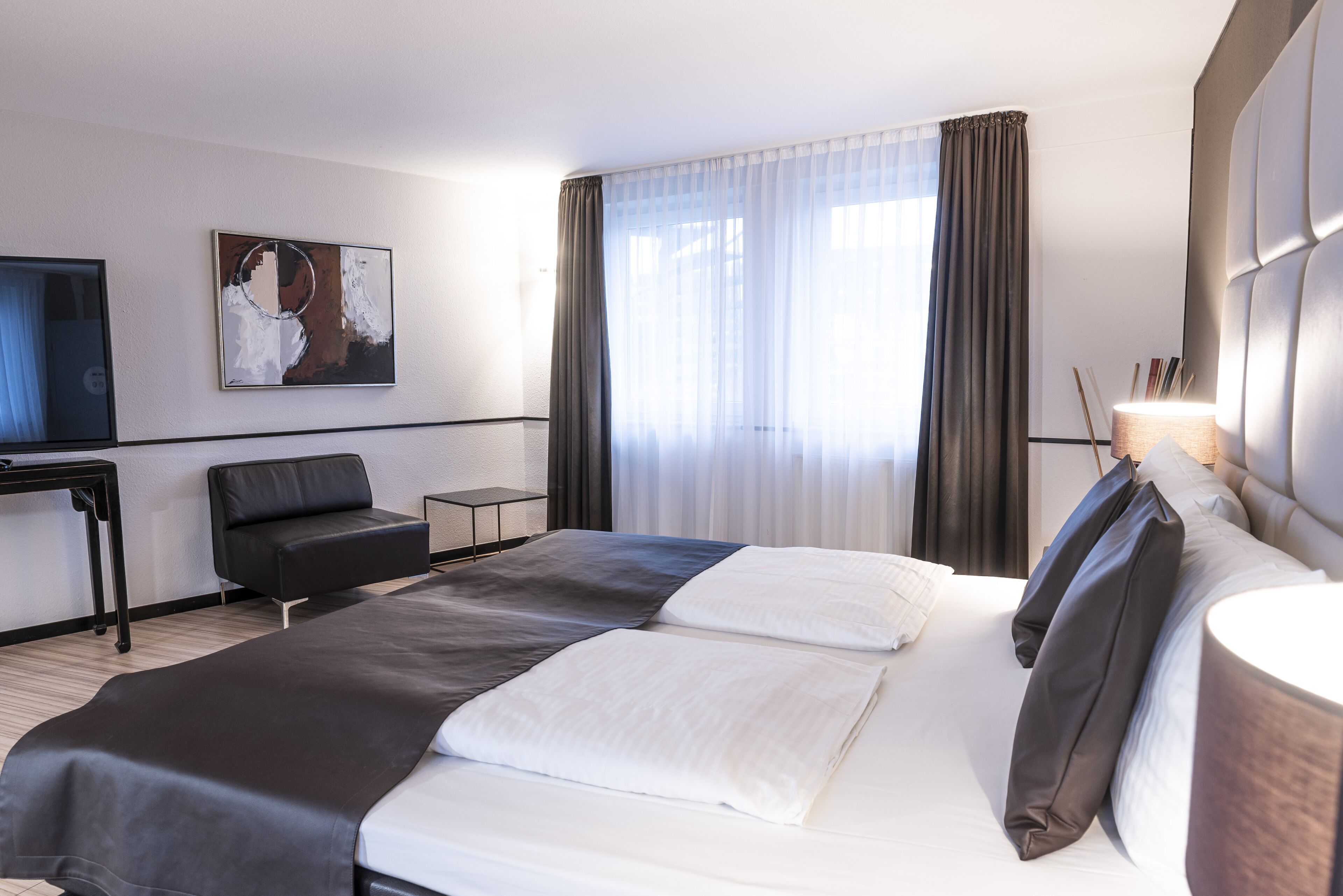 A modern hotel room with a large bed, a desk, a chair, and a television.
