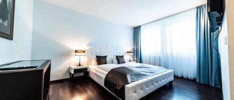 A modern hotel room with a large bed, a desk, and a chair.