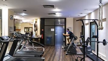 Un gimnasio con cintas de correr, un banco de pesas y una banca para levantamiento de pesas.