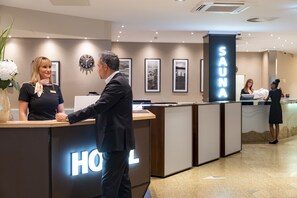 Zona de recepción de hotel con mostrador, un reloj, cuadros en la pared y señalización para sauna.