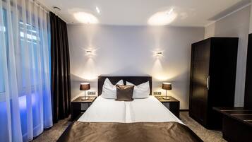 Hotelkamer met een groot bed, twee nachtkastjes, een kledingkast en uitzicht op het groen door dunne gordijnen.