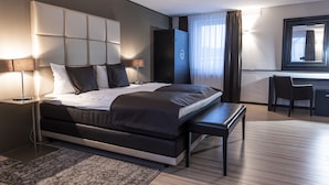 A modern hotel room with a large bed, bedside tables, a desk, and a chair. - Mauritius Hotel & Therme (Cologne)