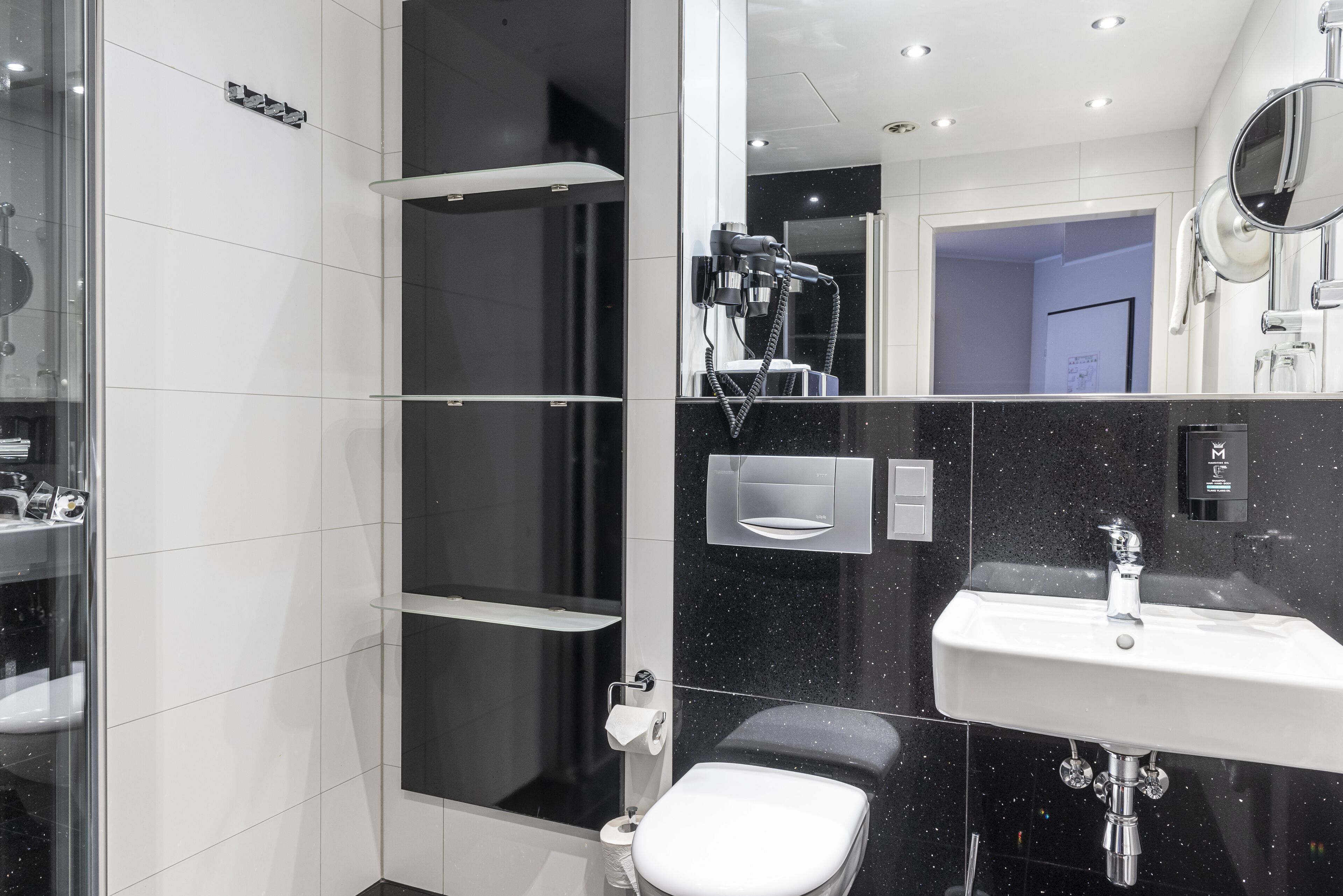 Ein modernes Badezimmer mit einer Duschkabine aus Glas, einer weißen Toilette, einem Waschbecken mit Spiegel und einer Wand aus schwarzen Fliesen.