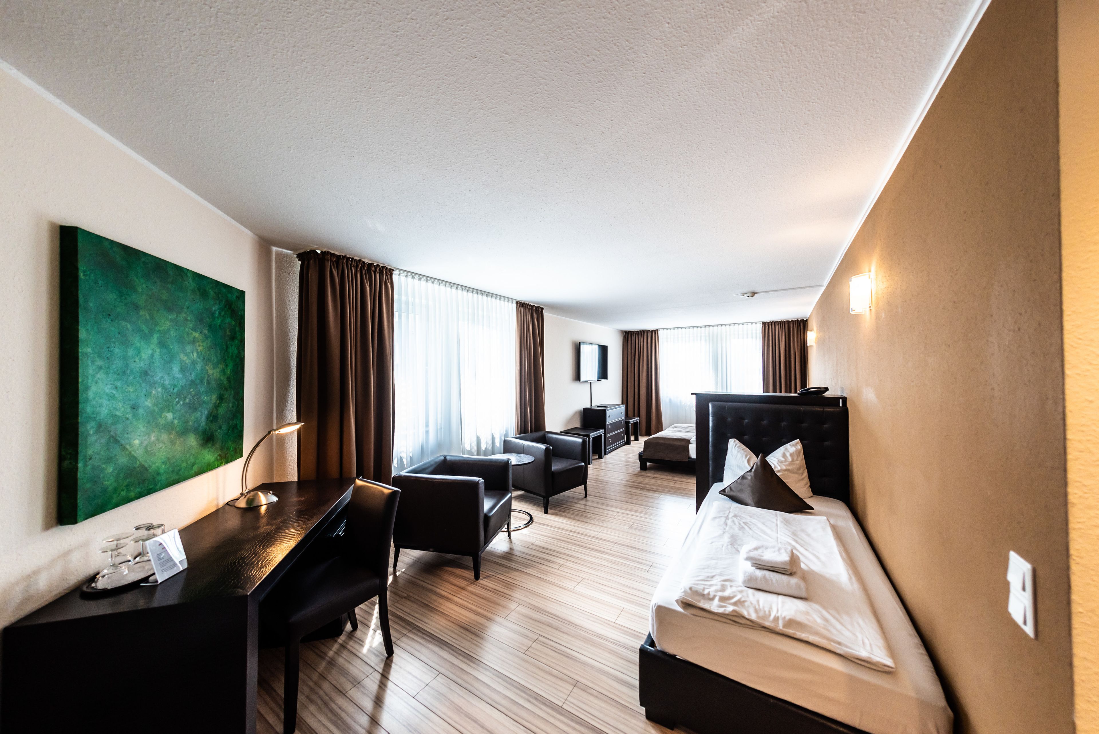 A hotel room with a bed, a desk, a chair, a sofa, and a large green painting on the wall.