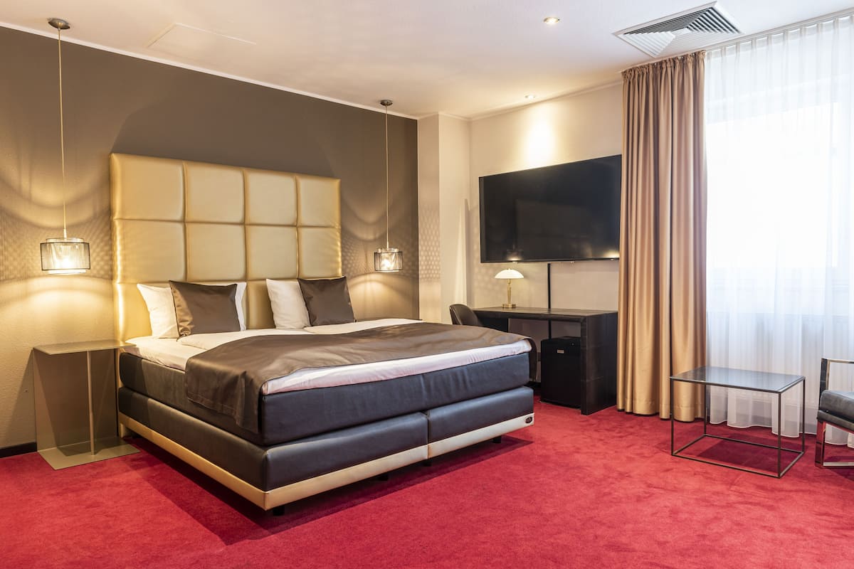 Une chambre d’hôtel moderne avec un grand lit, un bureau, une télévision et une moquette rouge.