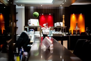 Un interior de restaurante con una barra pulida, un sombrero de chef en un soporte y una pared de acento roja.