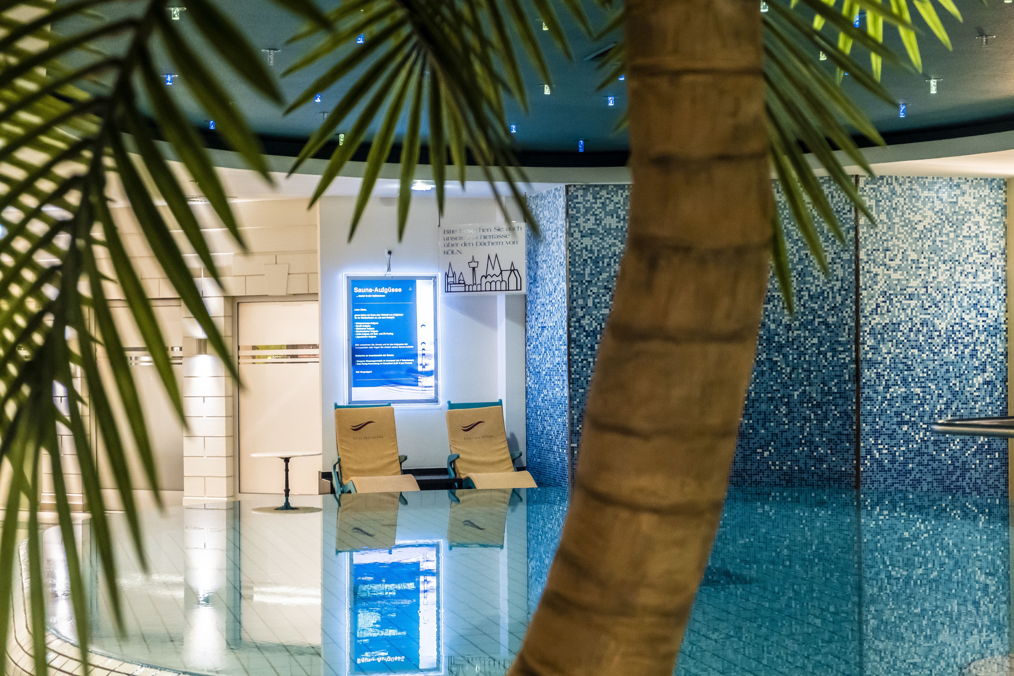 Uma área interna de piscina moderna, com piso de vidro, assentos próximos à piscina e painéis informativos.
