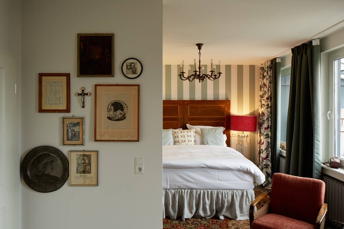 Un dormitorio con cama, un candelabro, una silla y varias fotografías enmarcadas en la pared.