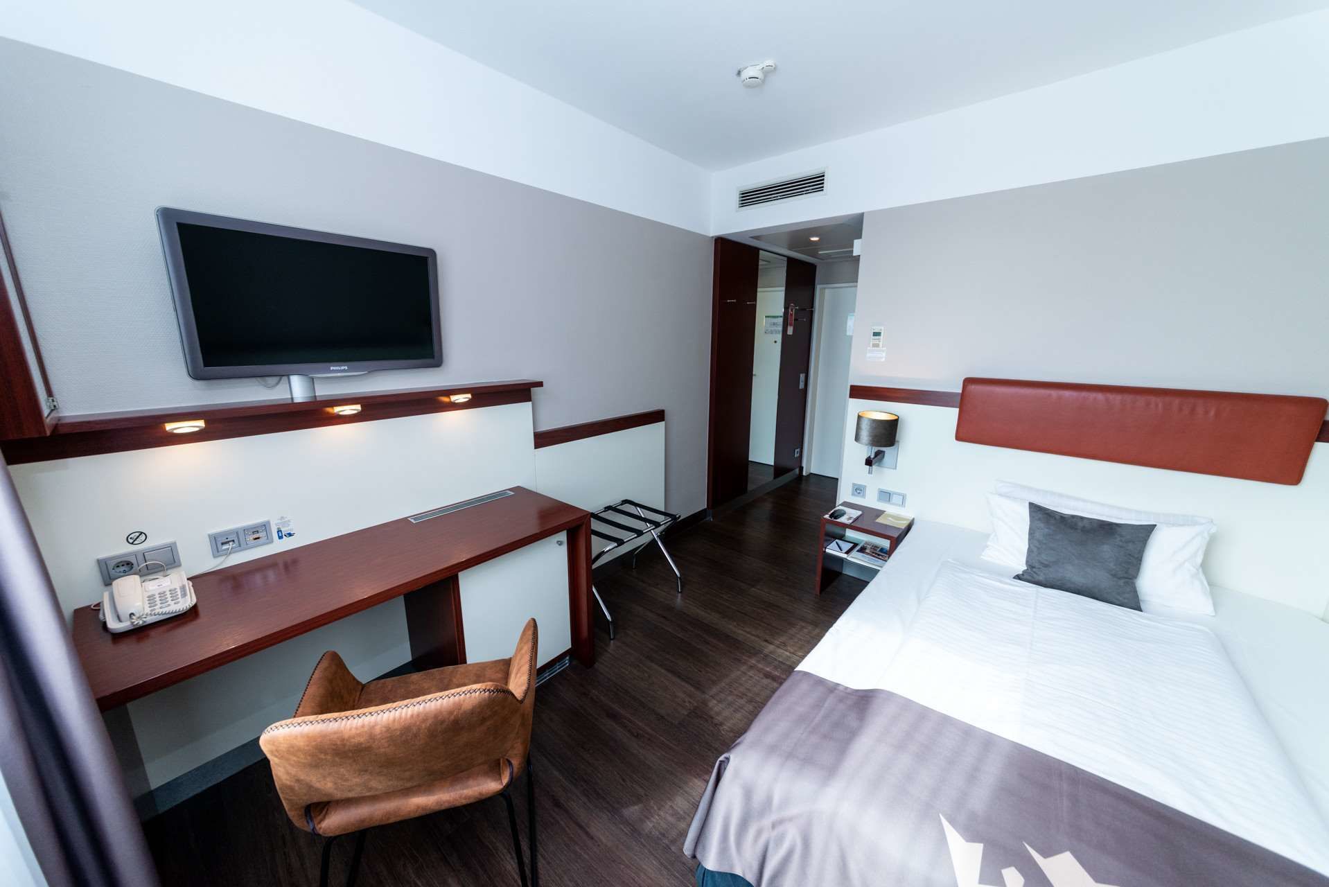 A hotel room with a bed, a desk with a chair, a television, and a telephone.
